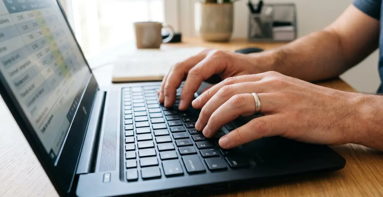 Gros plan sur des mains tapant sur un clavier d'ordinateur portable avec un tableau financier flouté en arrière-plan