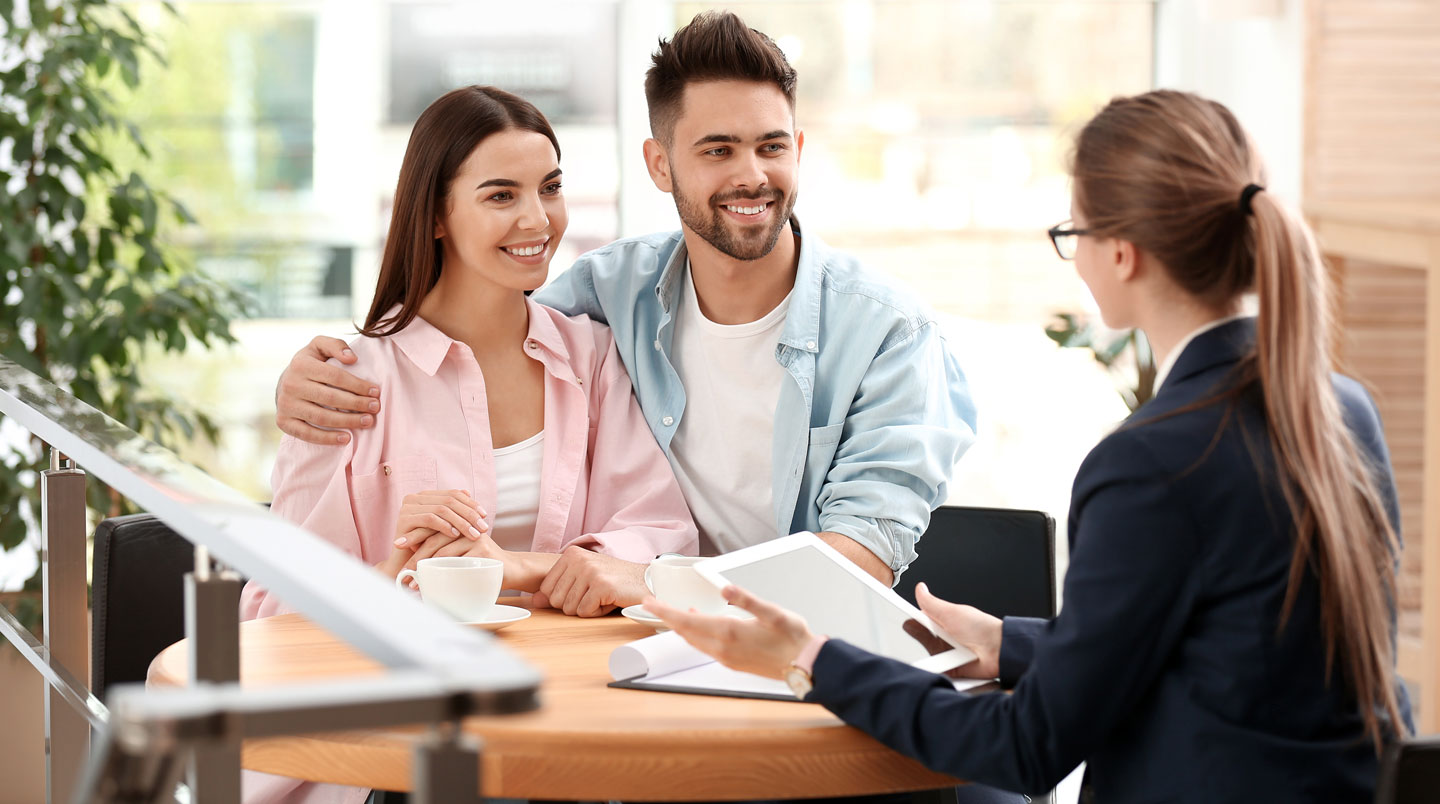 Vue en plongée sur une table de travail avec plusieurs devis d'assurance emprunteur étalés, main annotant un document, calculatrice et notes comparatives visibles
